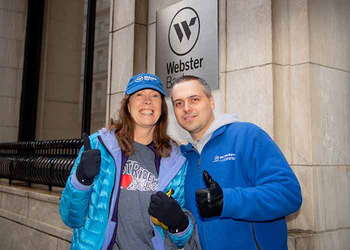 Two people stand outside Webster Bank giving a thumbs up